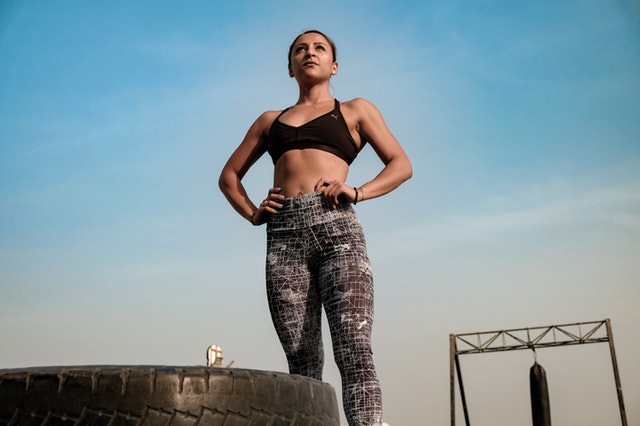 Žena s vyšportovanou postavou stojí vedľa pneumatiky v športovom oblečení